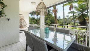 A balcony with wicker furniture, a glass table, and a hanging light fixture. - Top Floor Retreat – Walk to Beach & Town (Port Douglas)