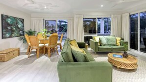 A modern living room with a green sofa, a dining table with chairs, and a large window with curtains. - Top Floor Retreat – Walk to Beach & Town (Port Douglas)