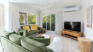A modern living room with a green sofa, a flat-screen TV, and large windows. - Top Floor Retreat – Walk to Beach & Town (Port Douglas)