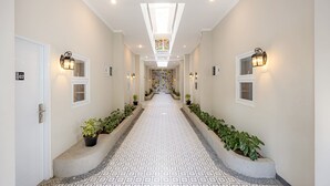 A hotel hallway with a patterned floor, potted plants, and wall-mounted lights. - Cove Nuansa Home (Jimbaran)