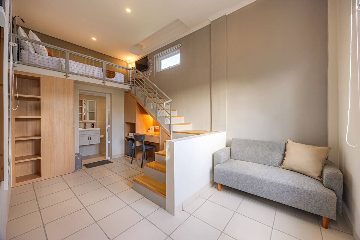 A modern interior with a staircase leading to a loft bedroom, a grey sofa, and a small desk area.