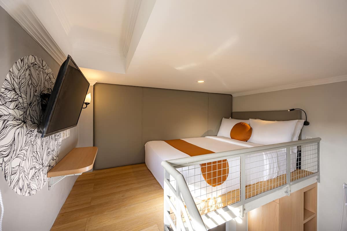 A modern bedroom with a bed, a TV mounted on the wall, and a wooden shelf.
