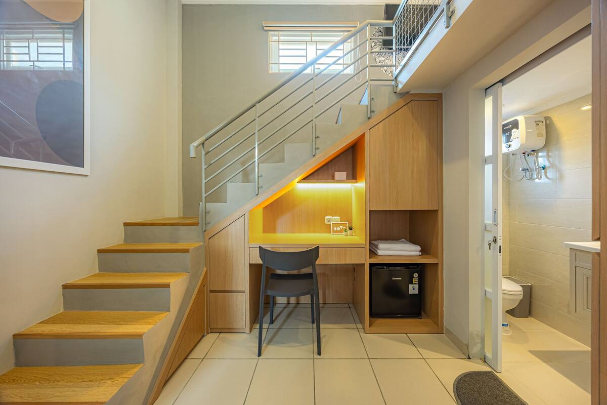 A compact kitchen with a built-in desk and chair, a refrigerator, and a small sink.
