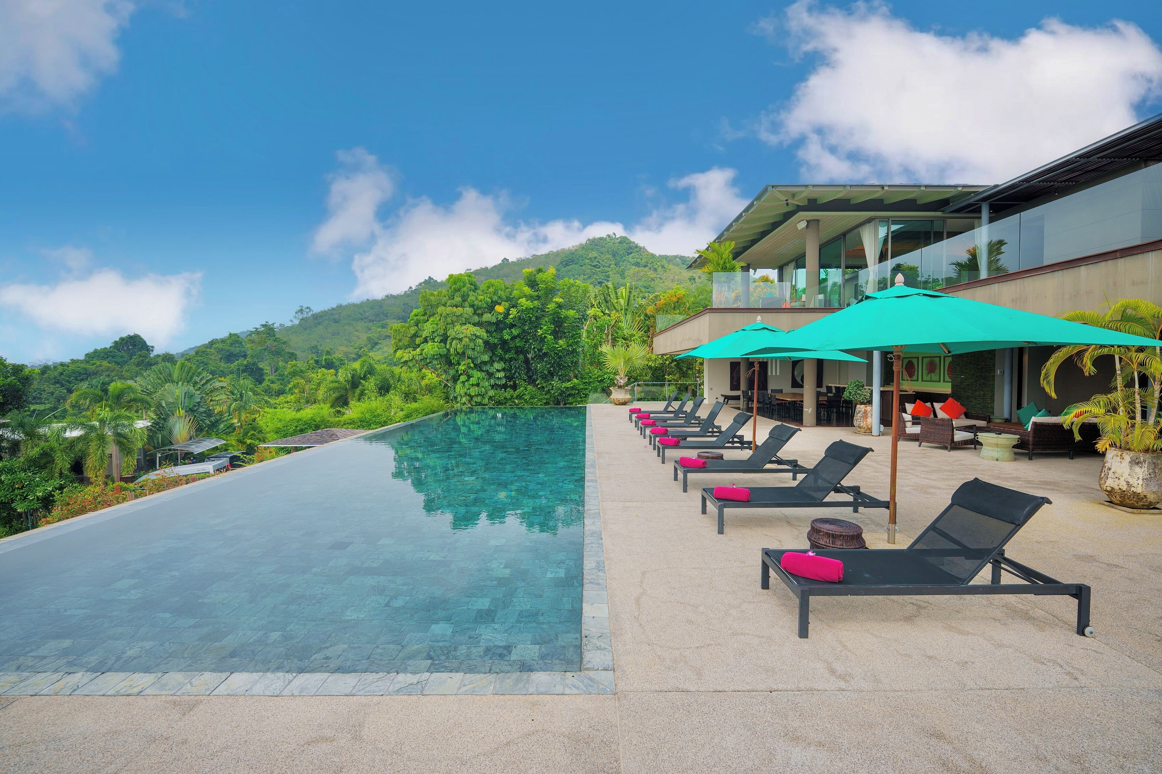 A infinity pool with lounge chairs and umbrellas, surrounded by lush greenery and a mountain backdrop.
