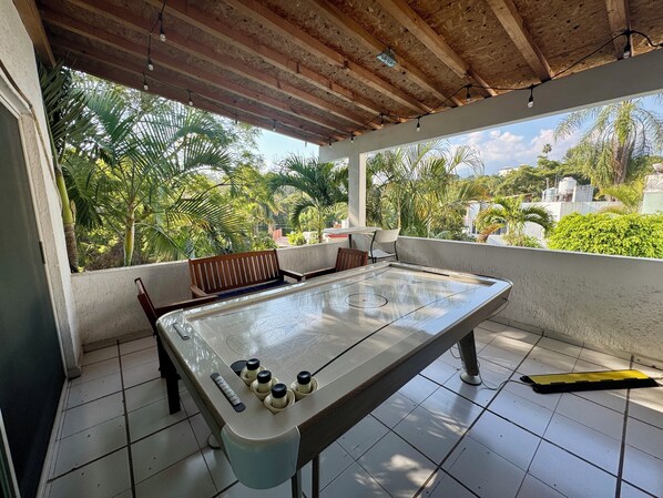 A pool table in a covered outdoor area with a view of greenery and buildings.