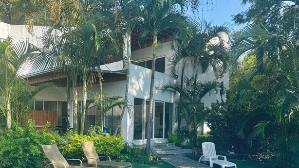 Un espace aménagé au bord de la piscine, avec des chaises longues, une piscine et une maison moderne dotée de grandes fenêtres et d’un patio couvert.