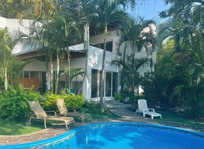 A poolside area with lounge chairs, a swimming pool, and a modern house with large windows and a covered patio.