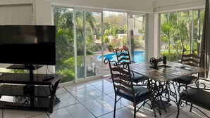 Un balcon spacieux avec vue sur la piscine, un coin repas avec une table et des chaises, et un téléviseur posé sur un meuble.