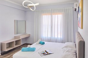 A hotel room with a bed, a bedside table, a mirror, a window with curtains, and a ceiling light fixture.