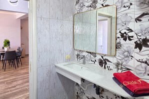 A hotel bathroom with a white sink, a mirror, and floral wallpaper.