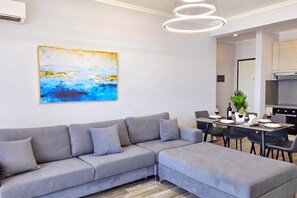 A modern living room with a grey sectional sofa, a dining table with chairs, and a painting on the wall. - Beachfront & Sea View Apartment 101, Durres, Albania (Durres)