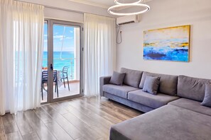 A modern living room with a grey sofa, a dining area with chairs, and a large window with curtains.