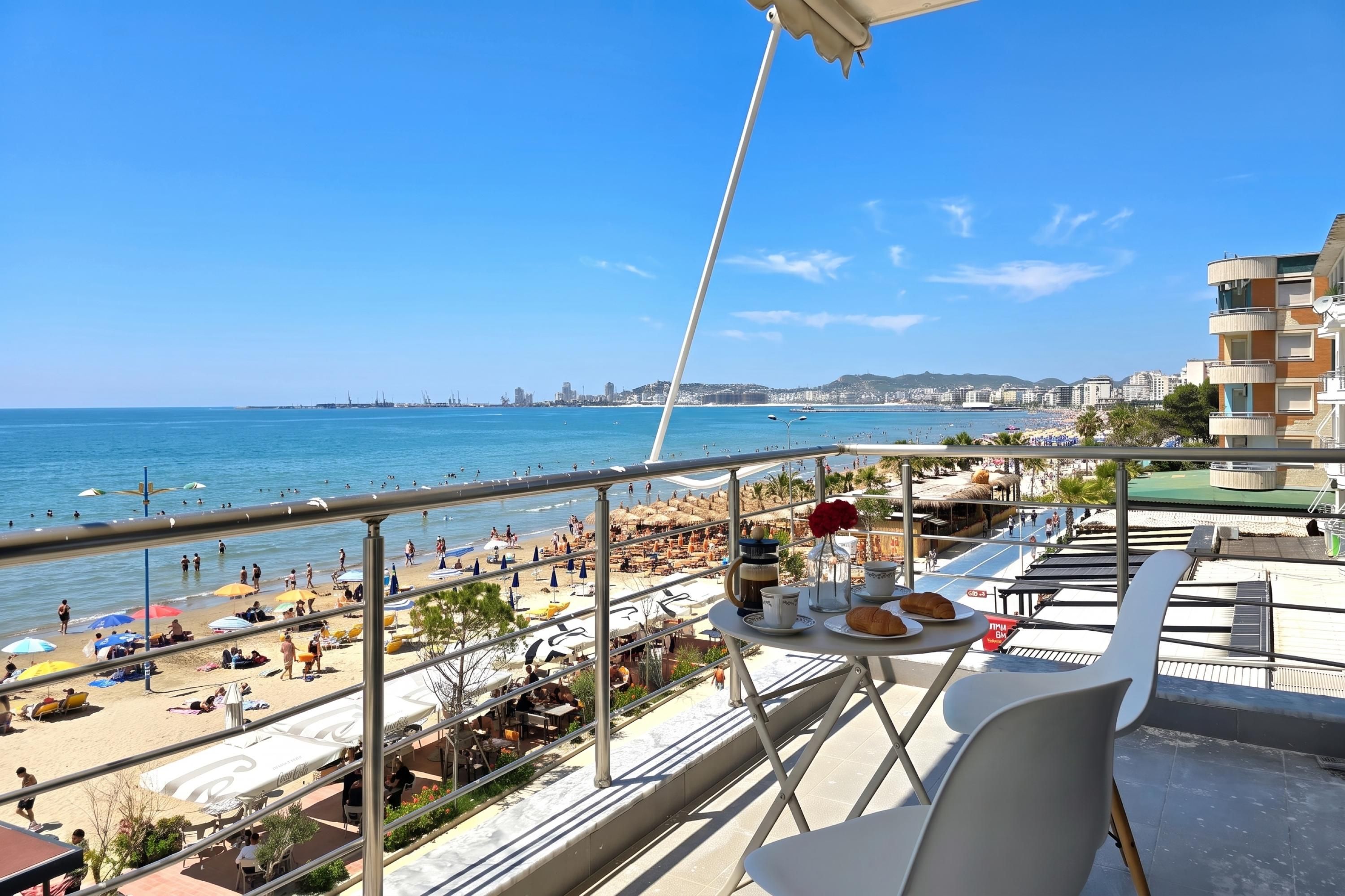 A balcony with a table set for breakfast overlooking a beach.