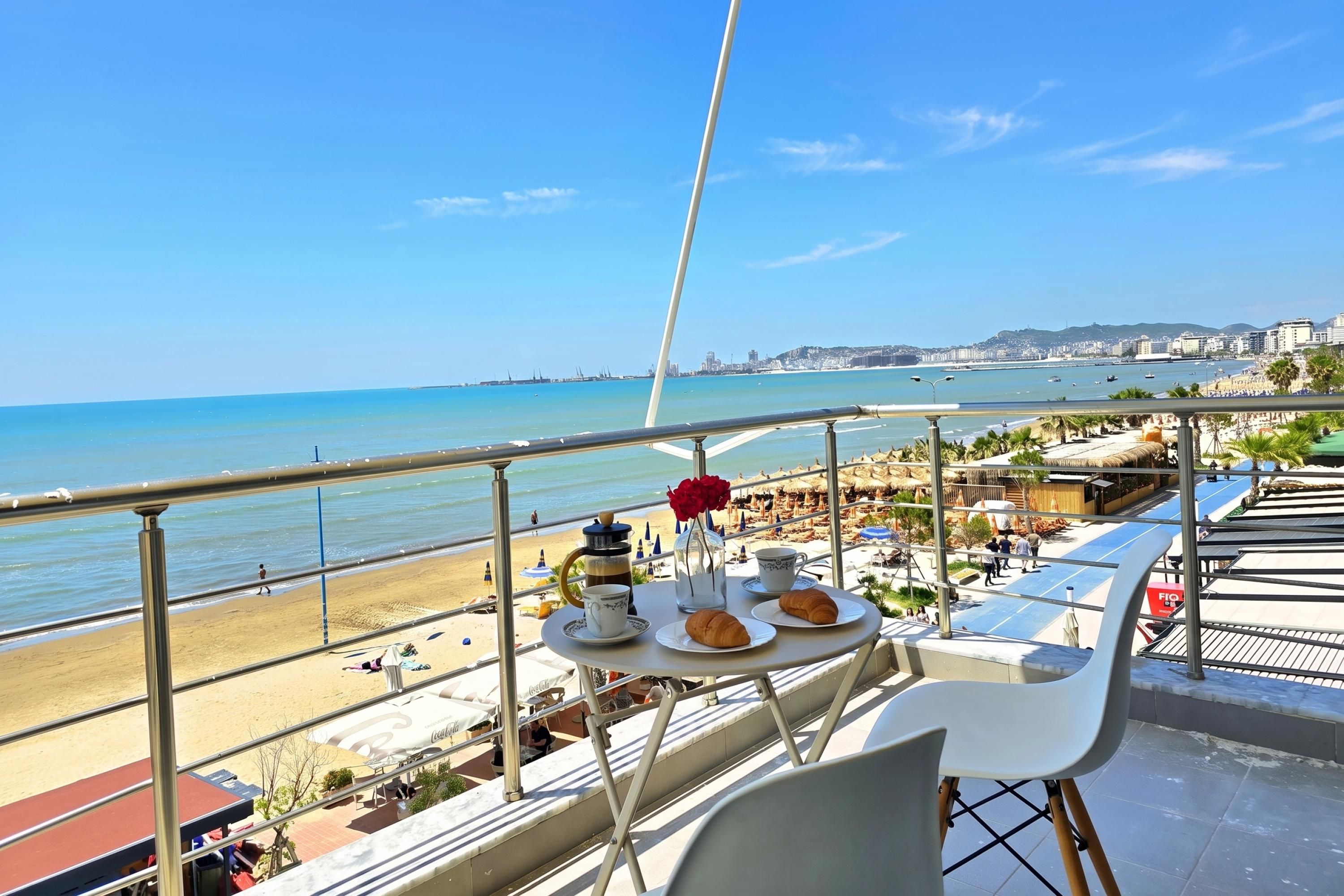 A balcony with a table set for two, overlooking a beach and cityscape.