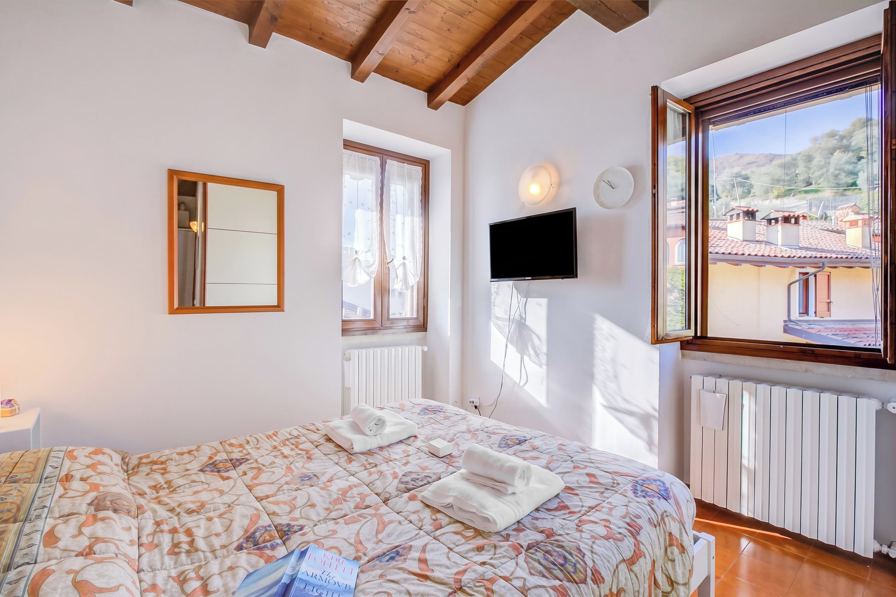 A bedroom with a bed, a TV, a window, and a radiator.