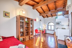 A spacious living area with a wooden ceiling, a dining table with red chairs, a kitchen with white cabinets, and a bookshelf. - Le Fontane With View Lake, Gardone Riviera, Italy (Gardone Riviera)