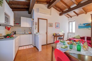 A kitchen with white cabinets, a microwave, and a dining area with a table set for two. - Le Fontane With View Lake, Gardone Riviera, Italy (Gardone Riviera)