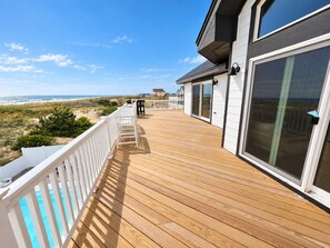 A wooden deck with a view of the beach, a pool, and a house with large windows. - Ocean front oasis full remodel hot tub heated pool Wild horses 8 bed 8 bath (Corolla)