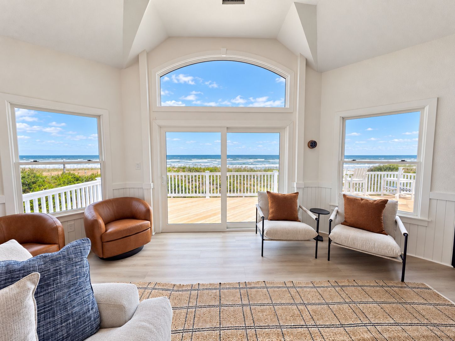 A spacious room with a large bay window, a wooden deck, and a view of the ocean.
