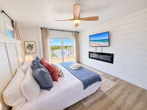 A bedroom with a bed, a ceiling fan, a television, and a view of the beach through the window. - Ocean front oasis full remodel hot tub heated pool Wild horses 8 bed 8 bath (Corolla)