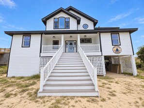 A two-story house with a front porch and a staircase leading to the entrance. - Ocean front oasis full remodel hot tub heated pool Wild horses 8 bed 8 bath (Corolla)