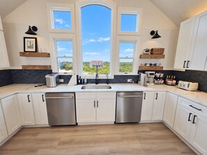 A modern kitchen with a large window, built-in appliances, and a view of greenery. - Ocean front oasis full remodel hot tub heated pool Wild horses 8 bed 8 bath (Corolla)