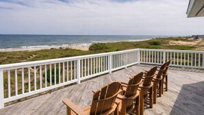 A wooden deck with a white railing, featuring four wooden chairs and a table, overlooking a beach and ocean. - Ocean front oasis full remodel hot tub heated pool Wild horses 8 bed 8 bath (Corolla)
