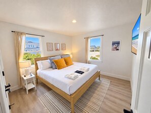 A bedroom with a wooden bed, a bedside table, a nightstand, a window with curtains, and a view of the outside. - Ocean front oasis full remodel hot tub heated pool Wild horses 8 bed 8 bath (Corolla)