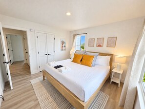 A well-lit bedroom with a large bed, bedside tables, and a view of the outdoors. - Ocean front oasis full remodel hot tub heated pool Wild horses 8 bed 8 bath (Corolla)