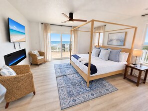 A bedroom with a four-poster bed, a television, a wicker chair, a nightstand, and a view of the beach. - Ocean front oasis full remodel hot tub heated pool Wild horses 8 bed 8 bath (Corolla)
