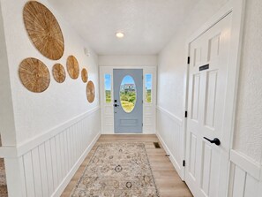 A hallway with a patterned rug, white wainscoting, and a door with a view of a landscape. - Ocean front oasis full remodel hot tub heated pool Wild horses 8 bed 8 bath (Corolla)