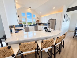 A modern kitchen with a large island, white cabinetry, and a view of the outdoors. - Ocean front oasis full remodel hot tub heated pool Wild horses 8 bed 8 bath (Corolla)