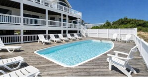 A multi-story building with a pool area, including a wooden deck and white lounge chairs. - Ocean front oasis full remodel hot tub heated pool Wild horses 8 bed 8 bath (Corolla)