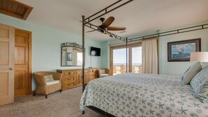 A bedroom with a bed, a wooden dresser, a wicker chair, a ceiling fan, a TV, and a window with a view. - Ocean front oasis full remodel hot tub heated pool Wild horses 8 bed 8 bath (Corolla)