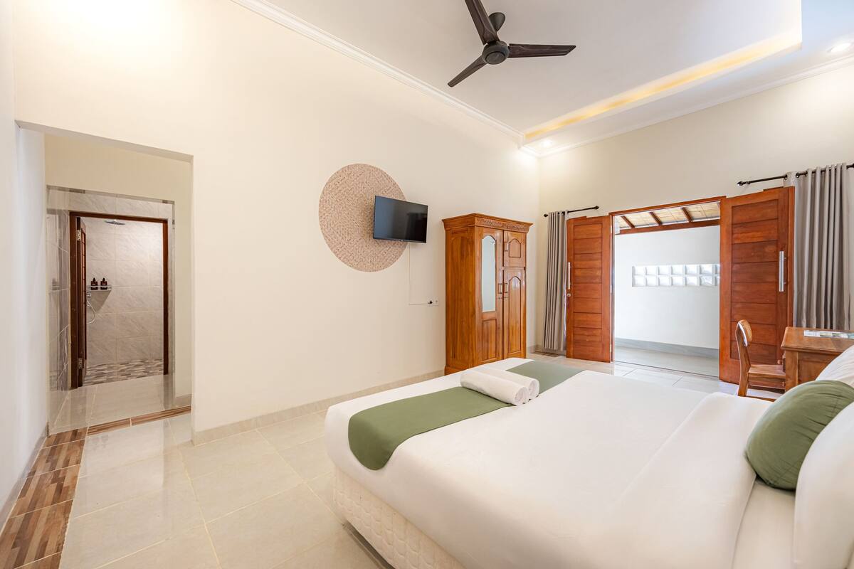 A hotel room with a bed, a TV, a ceiling fan, and a wooden wardrobe.