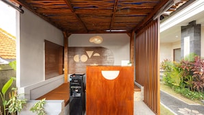 A reception area with a wooden desk, a water dispenser, and a wall with geometric shapes. - Cove Cubang Homestay (Kutuh)