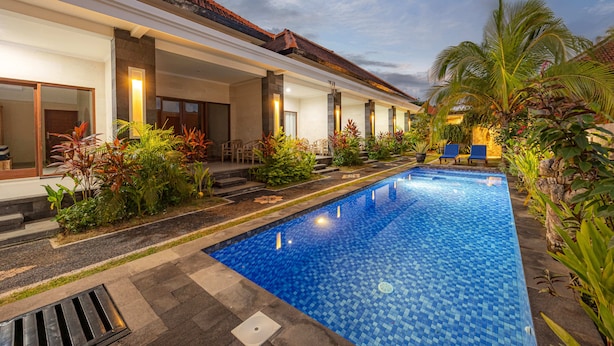 A swimming pool with a tiled edge, surrounded by plants and a building with large windows. - Cove Cubang Homestay (Kutuh)