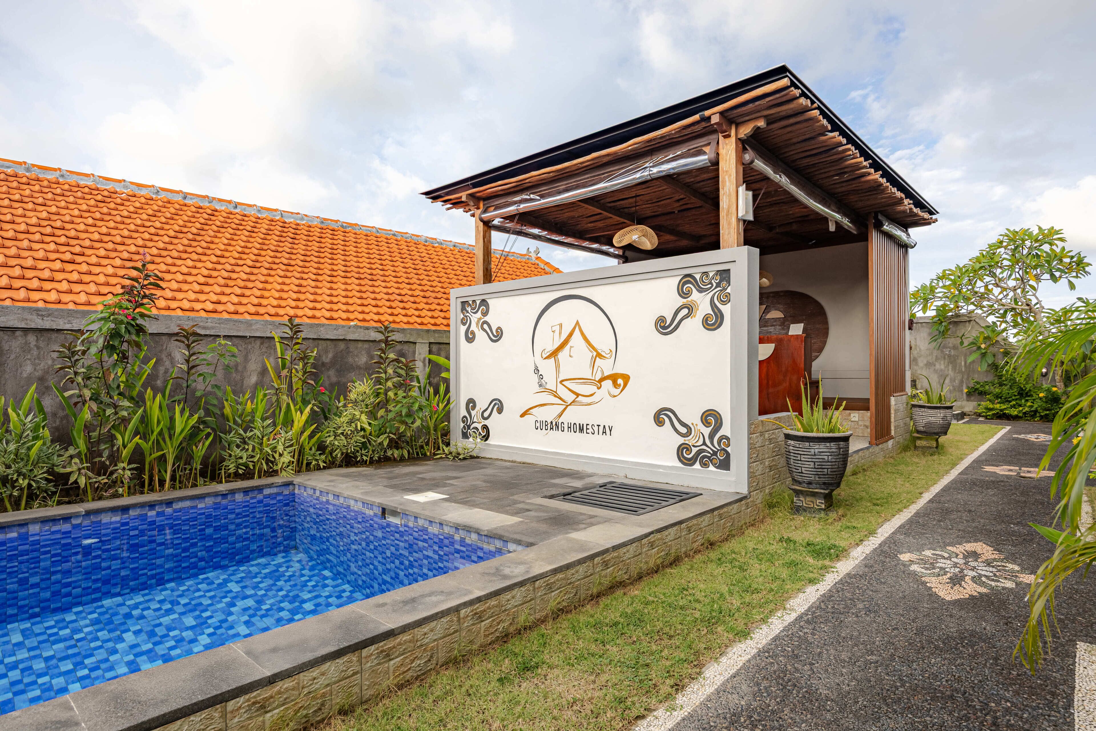 Una piscina con azulejos azules, una pérgola de madera y una pared con un logotipo y texto.