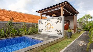Una piscina con azulejos azules, una pérgola de madera y una pared con un logotipo y texto.