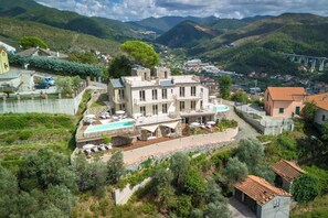 A large, multi-story building with a pool and outdoor seating, surrounded by greenery and mountains. - Relais Le Torri in Verici Punta Manara, Casarza Ligure, Italy (Casarza Ligure)