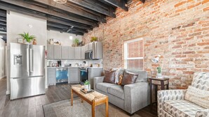 Eine moderne Küche mit Edelstahlgeräten, einem grauen Sofa und einem gemusterten Sessel.