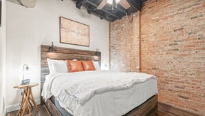 Ein Schlafzimmer mit einem hölzernen Bett, einer Ziegelwand und einem kleinen Tisch mit einer Lampe.