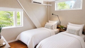 Une chambre avec deux lits, une table de chevet, une lampe et une fenêtre donnant sur des arbres.