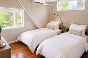 Une chambre avec deux lits, une table de chevet, une lampe et une fenêtre donnant sur des arbres.