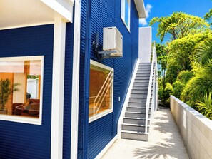 Une maison bleue avec un escalier menant à un balcon, entourée d’une végétation luxuriante.