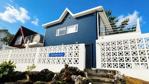 A blue building with a sign reading 'NAKAMA VILLA,' a white fence with a geometric pattern, and a clear blue sky. - A Premium Okinawa Villa Stay with Sauna & Jacuzzi (nakama, Onna Village)