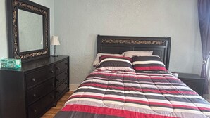 A bedroom with a bed, a dresser, a mirror, and a nightstand.