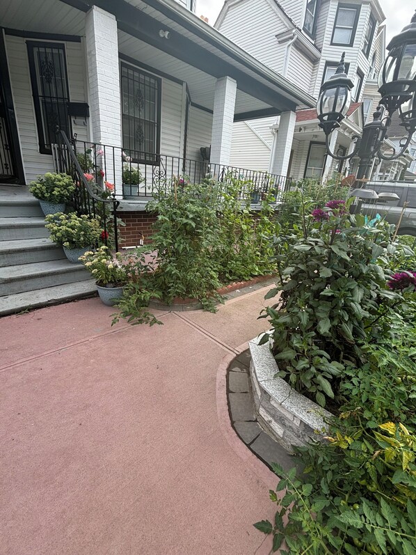 A residential building with a front porch, steps, potted plants, and a brick pathway.