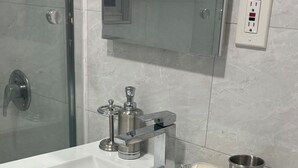A bathroom with a white sink, a glass shower enclosure, a mirror, and a wall-mounted electrical outlet.
