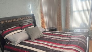 A bed with a striped bedspread, a headboard with a decorative pattern, and a bedside table with a lamp.
